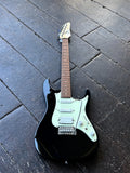 A black Ibanez electric guitar with a pale mint green pickguard and maple neck, photographed from above on a dark wooden plank floor.