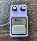 An Ibanez OSC Stereo Chorus guitar effect pedal in light purple with black and silver knobs and a silver footswitch, resting on a textured dark brown surface.