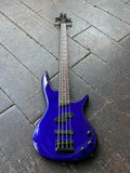 An Ibanez blue electric bass guitar with a glossy metallic finish, resting diagonally on a dark wooden plank floor.