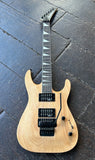 A Jackson Dinkey natural wood electric guitar with black hardware, two humbucker pick ups, shown from a top-down view on a dark wooden floor.