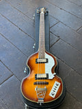 A double-cutaway electric guitar with a sunburst finish, resting inside a black hard case on a dark wooden floor.