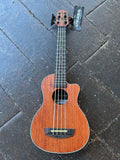 A four-string U-Bass guitar with reddish-brown wood finish, black neck, and black headstock, photographed from above on dark stone tiles. A black 'UBASS' brand tag is attached to the headstock.