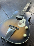 Acoustic guitar with a visible brand logo on a dark wooden floor