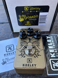 Keeley Electronics El Rey Dorado Overdrive guitar pedal shown with its retail box and accessories on a dark wooden surface.