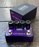 An MXR Sub Machine guitar effects pedal in metallic purple, shown with its black and purple retail box on a dark wooden surface. The pedal features four black control knobs (Volume, Tone, Fuzz, Sub) and two silver footswitches.