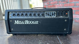 A black Mesa/Boogie guitar amplifier head sitting on a stone surface with a brick wall and railing in the background.