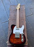 A Michael Kelly classic Telecaster style electric guitar with a dark brown sunburst finish, resting on top of its textured brown hard case on dark wooden planks.