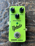 A bright lime green Nobels ODR-mini guitar effects pedal with three black knobs, a silver footswitch, and a green indicator light, photographed on a textured dark stone surface.