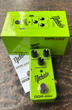 A bright lime green Nobels ODR-mini guitar effects pedal with black knobs and a silver footswitch, shown in front of its matching lime green retail box and a small white instruction booklet on a dark wood surface.