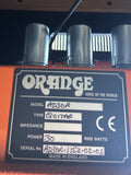 Close-up of an Orange AD306 guitar pedal or amplifier component, showing the orange casing, three silver metal canisters, and a black specification plate with handwritten model details.