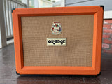 Orange guitar amplifier on a wooden floor with a blurred background