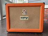 Orange guitar amplifier on a wooden floor with a blurred background