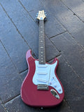 A PRS SE guitar Dragon Fruit red finish with white pickguard and chrome hardware, resting diagonally on dark wooden planks.red 