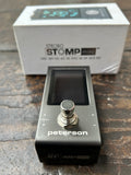 Grey Peterson Strobo Stomp mini guitar effects pedal on a wooden surface with its packaging in the background.