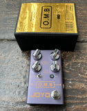 JOYO O.M.B lavender guitar effects pedal with four control knobs on a wooden surface with its packaging above.
