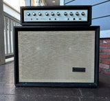 A vintage Silvertone black speaker cabinet with a beige mesh grille and a matching head amplifier stacked on top, photographed outdoors on a porch with a brick wall and siding in the background.