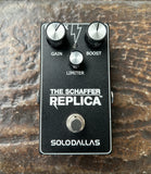 A black Solodallas 'The Schaffer Replica' guitar effects pedal with silver knobs and white lettering, photographed from directly above on a textured brown wooden surface.