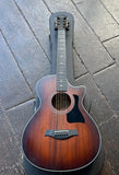 A Taylor 322ce  acoustic guitar with a dark brown sunburst finish, ebony e its black protective hard case on a dark wooden plank floor.