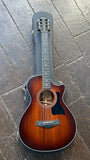 A Taylor 322ce  acoustic guitar with a dark brown sunburst finish, ebony e its black protective hard case on a dark wooden plank floor.