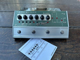 Tech 21 NYC SansAmps VT Bass Deluxe guitar effects pedal with a green and silver faceplate, shown on a dark wooden surface with its user manual in front.