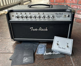 Black Two-Rock amplifier head and pedal on a wooden surface with a brick wall background