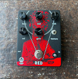 A Walrus audio black and red Music Man 'Red' guitar effects pedal with six black knobs, a silver footswitch, and a red graphic of a figure with a sword, photographed from directly above on a rustic wooden surface.