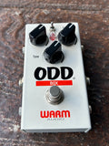grey Guitar effects pedal with 'ODD Box' and 'Warm Audio' branding owith three control knobs, on a rustic background