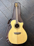 An Washburn  acoustic-electric guitar with a natural wood finish and a dark brown cutaway body, resting on a dark brown guitar case over a dark wooden floor.