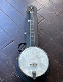 A banjo with a white front head,  silver metal hardware, ebony fretboard, resting on a black hard case over a dark wood plank floor.