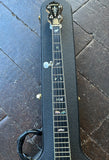 A close-up of a black guitar headstock and neck with decorative inlays, resting on a black hard case over a dark wooden floor.