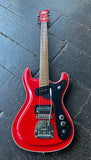 A red Wilson Brothers Ventures style electric guitar with a black pickguard and maple neck, photographed from above on a dark wooden plank floor.