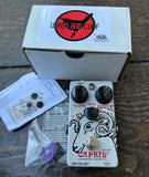 Grey Caprid guitar effects pedal with Wren and Cuff packaging on a wooden surface