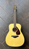A natural wood Yamaha acoustic twevle string guitar guitar with a dark tortoiseshell pickguard, resting on a dark rustic wooden plank floor.